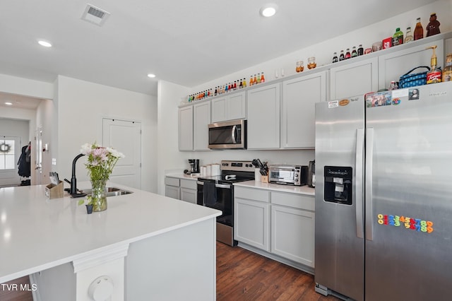 kitchen featuring stainless steel appliances, dark wood finished floors, light countertops, a sink, and recessed lighting