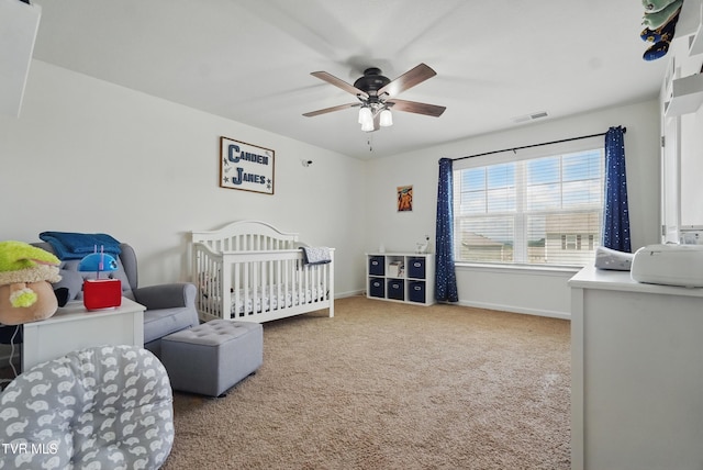 carpeted bedroom with baseboards, a crib, and a ceiling fan
