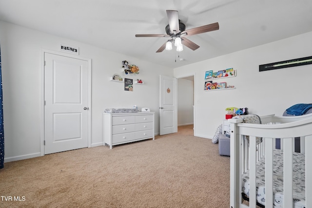 bedroom with light carpet, baseboards, ceiling fan, and a nursery area