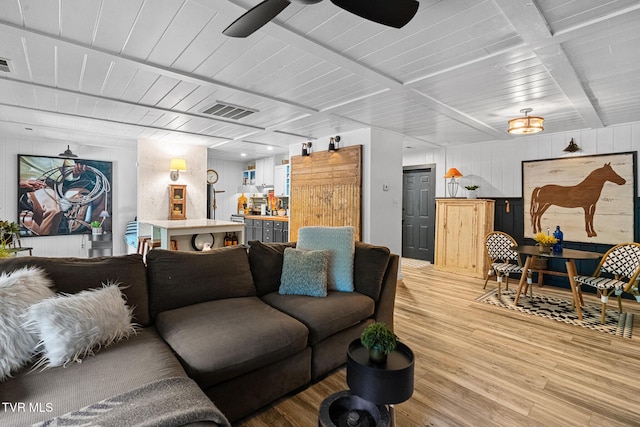 living room featuring light wood finished floors, a bar, a ceiling fan, beamed ceiling, and wood walls