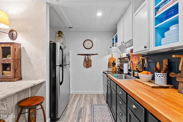 kitchen featuring appliances with stainless steel finishes, light wood-type flooring, baseboards, white cabinetry, and butcher block counters