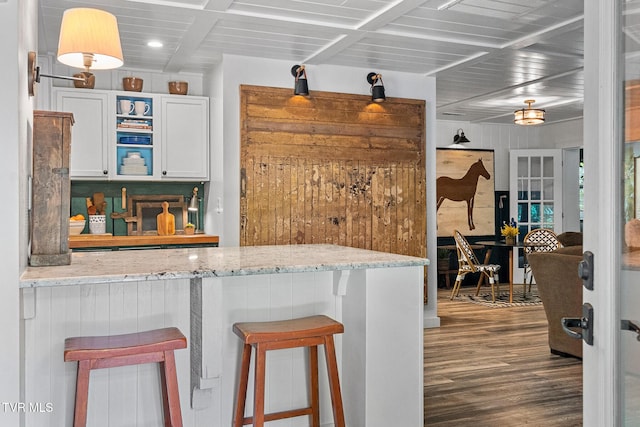 kitchen featuring wood finished floors, a breakfast bar, light stone countertops, white cabinetry, and recessed lighting