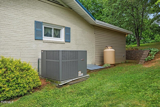 view of side of home with central AC, brick siding, and a lawn