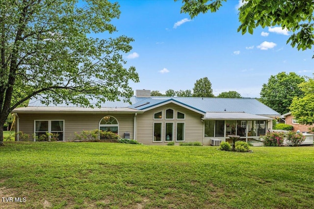 back of property featuring a sunroom, a chimney, a lawn, metal roof, and central air condition unit