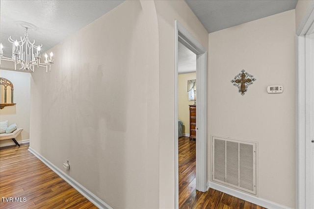 hall featuring wood finished floors, a chandelier, and baseboards