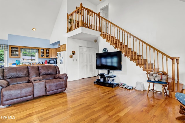 living area with high vaulted ceiling, light wood-style flooring, and stairway
