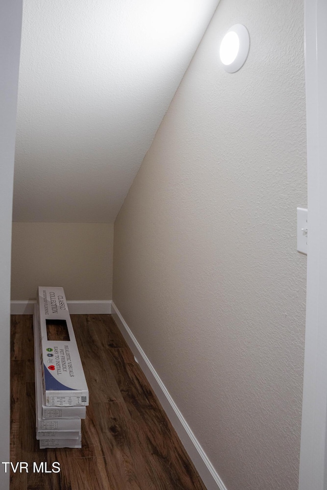 interior space featuring dark wood-style flooring, vaulted ceiling, and baseboards