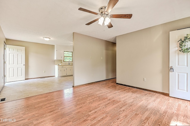 unfurnished living room with ceiling fan, light wood finished floors, a sink, and baseboards