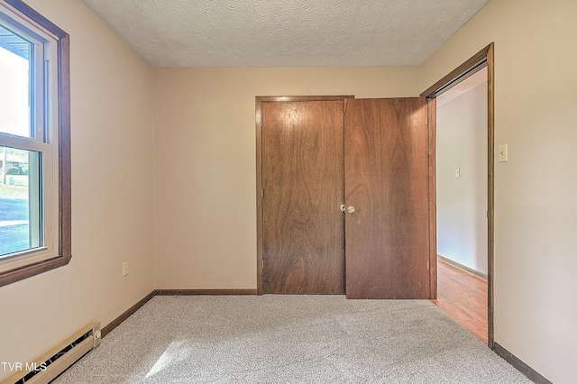 unfurnished bedroom with a baseboard heating unit, carpet flooring, a textured ceiling, and baseboards