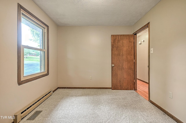 empty room with baseboard heating, a textured ceiling, carpet, and baseboards