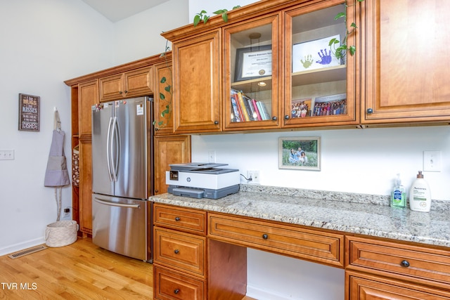 963 NE Woodlawn Ter, Abingdon, VA 24210 - kitchen with freestanding refrigerator, brown cabinetry, light wood-style floors, glass insert cabinets, and light stone countertops