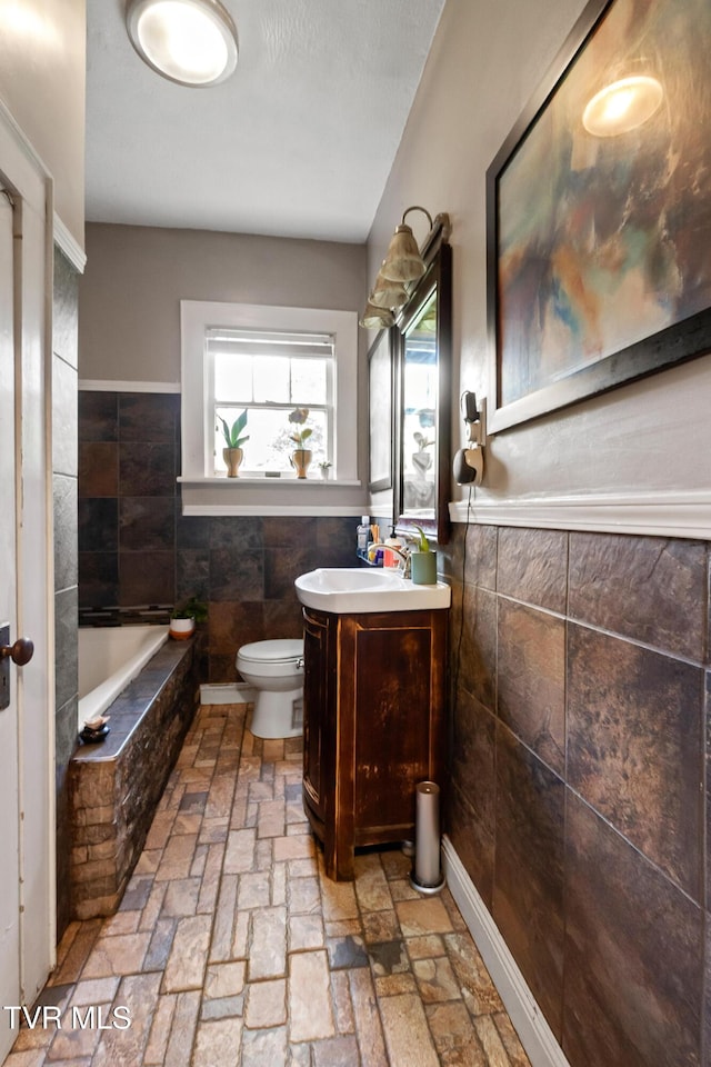 408 N Main St, Greeneville, TN 37745 - bathroom with tile walls, toilet, a wainscoted wall, vanity, and a relaxing tiled tub