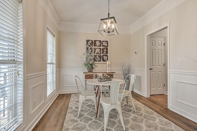 dining area with wood finished floors, a chandelier, a wainscoted wall, crown molding, and a decorative wall