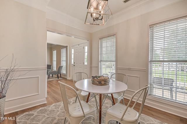 dining area with a chandelier, crown molding, wainscoting, light wood-type flooring, and a decorative wall