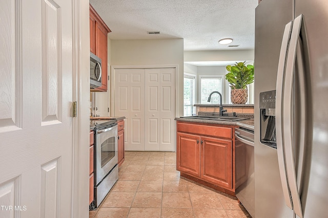 kitchen with stainless steel appliances, a sink, dark countertops, brown cabinets, and light tile patterned floors