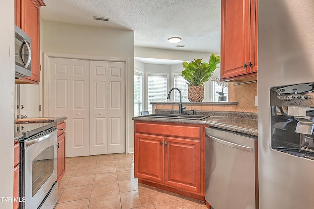 kitchen featuring stainless steel appliances, a sink, dark countertops, tasteful backsplash, and light tile patterned floors