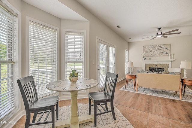 dining area featuring a ceiling fan, a fireplace, baseboards, and light tile patterned flooring