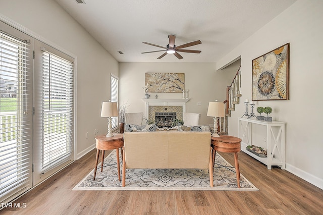 living room featuring ceiling fan, a fireplace, wood finished floors, baseboards, and stairway