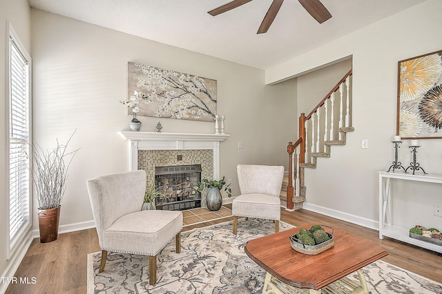 living area featuring a ceiling fan, a tiled fireplace, wood finished floors, and stairs