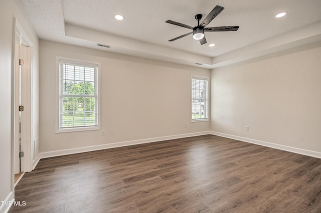 empty room featuring a tray ceiling, healthy amount of natural light, dark wood finished floors, and recessed lighting