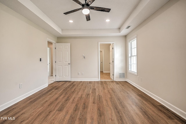 unfurnished bedroom featuring a raised ceiling, wood finished floors, recessed lighting, baseboards, and connected bathroom