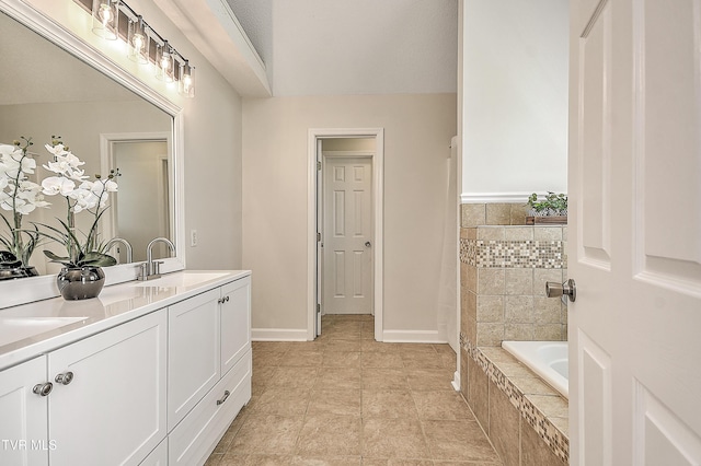 full bathroom with tiled tub, double vanity, and baseboards
