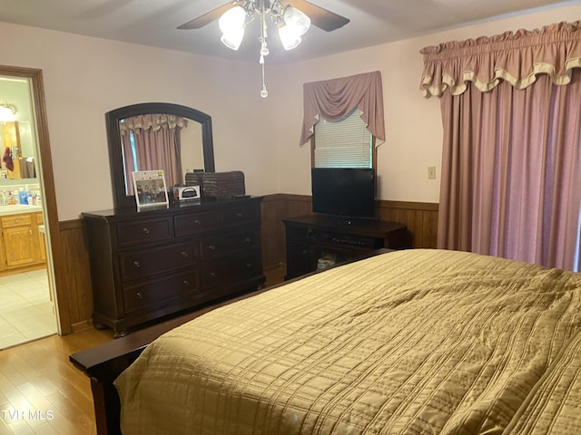 203 Oak Ln, Johnson City, TN 37604 - bedroom with wainscoting, light wood finished floors, wood walls, connected bathroom, and a ceiling fan