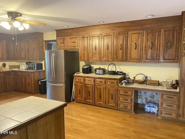 203 Oak Ln, Johnson City, TN 37604 - kitchen with freestanding refrigerator, tile counters, ceiling fan, brown cabinetry, and light wood-type flooring