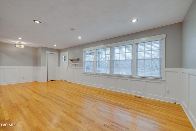 unfurnished living room featuring a decorative wall, light wood-style floors, wainscoting, and recessed lighting
