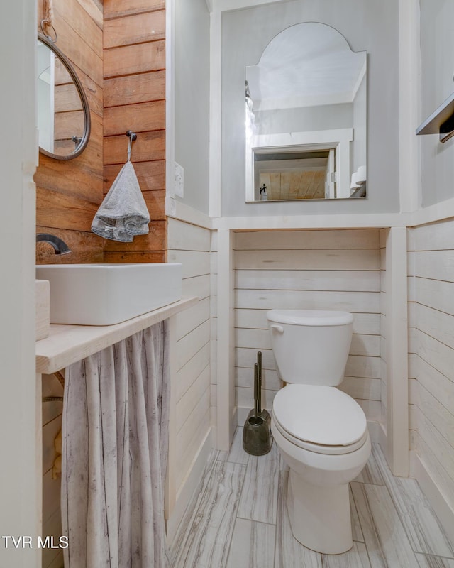 half bath with wooden walls, toilet, and a sink