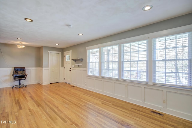 unfurnished living room featuring a decorative wall, light wood finished floors, wainscoting, and recessed lighting