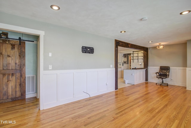 unfurnished room featuring a barn door, wainscoting, a decorative wall, light wood-style floors, and recessed lighting