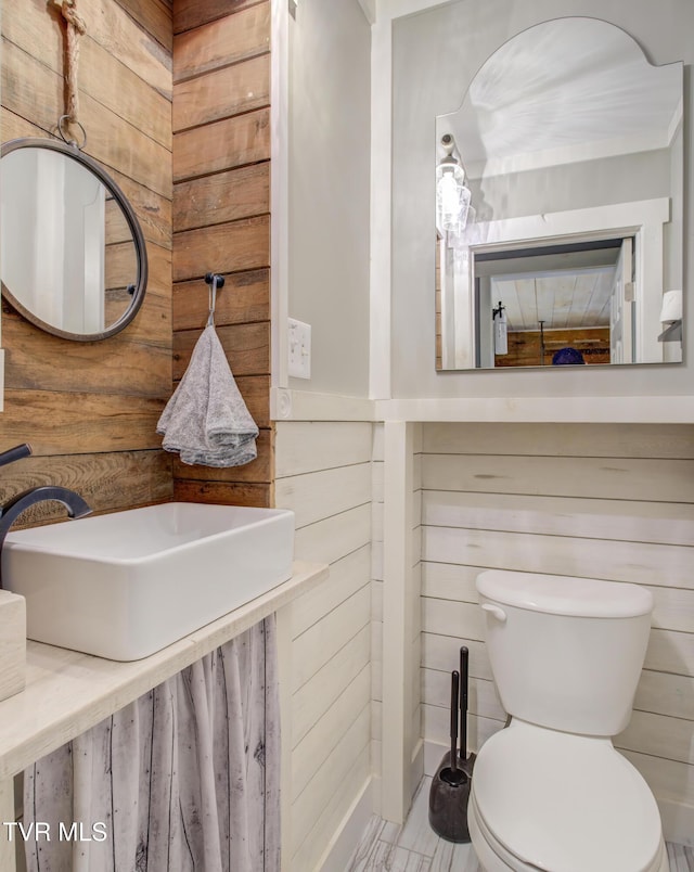 half bath featuring wood walls, toilet, and a sink