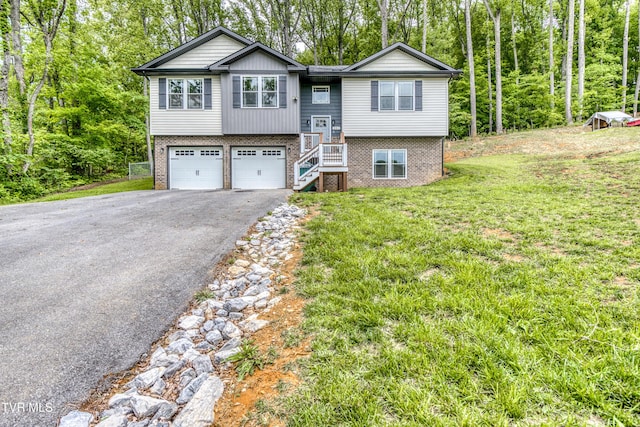 bi-level home with brick siding, asphalt driveway, a garage, a front yard, and stairs