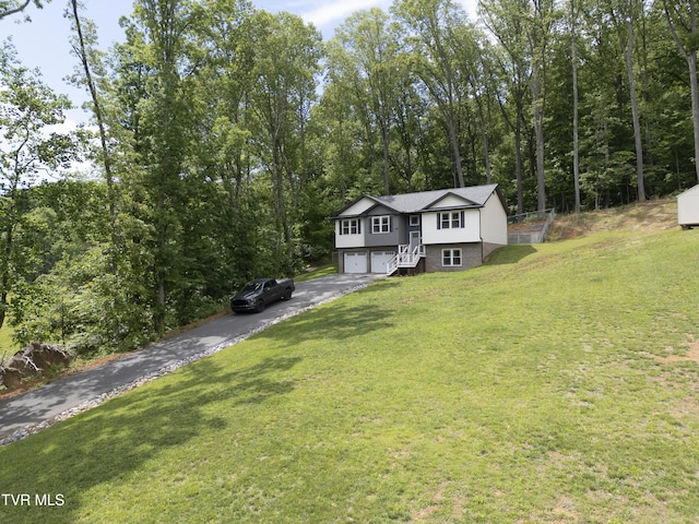 split foyer home with asphalt driveway, a garage, a front yard, and a forest view