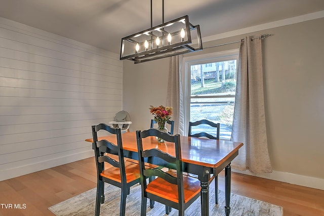 dining room with a chandelier, wood finished floors, baseboards, and wood walls