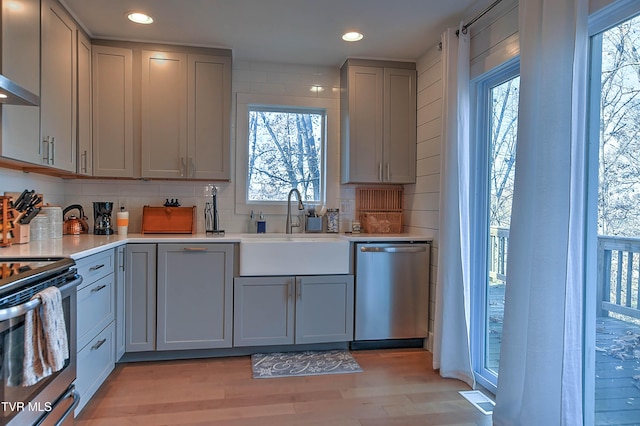 kitchen featuring stainless steel appliances, gray cabinetry, a sink, backsplash, and plenty of natural light