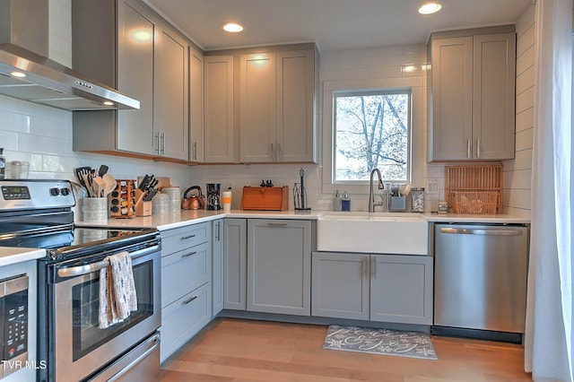 kitchen featuring stainless steel appliances, wall chimney exhaust hood, gray cabinetry, and recessed lighting