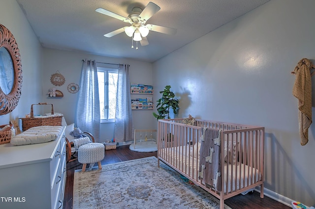 bedroom with wood finished floors, a nursery area, a ceiling fan, and baseboards
