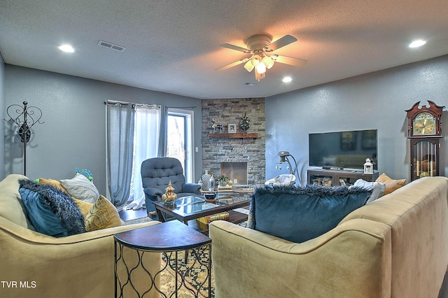 living area featuring a ceiling fan, a textured ceiling, recessed lighting, a stone fireplace, and a textured wall