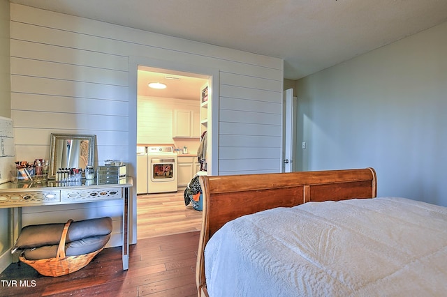 bedroom featuring hardwood / wood-style flooring, washing machine and dryer, and wooden walls