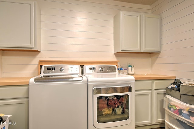 laundry area featuring separate washer and dryer, wood walls, and cabinet space