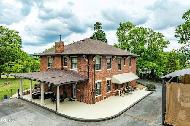2107 Bartlett St, Johnson City, TN 37601 - back of house with a chimney, brick siding, roof with shingles, an outdoor living space, and a patio