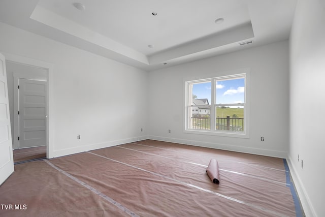 empty room featuring a raised ceiling and baseboards