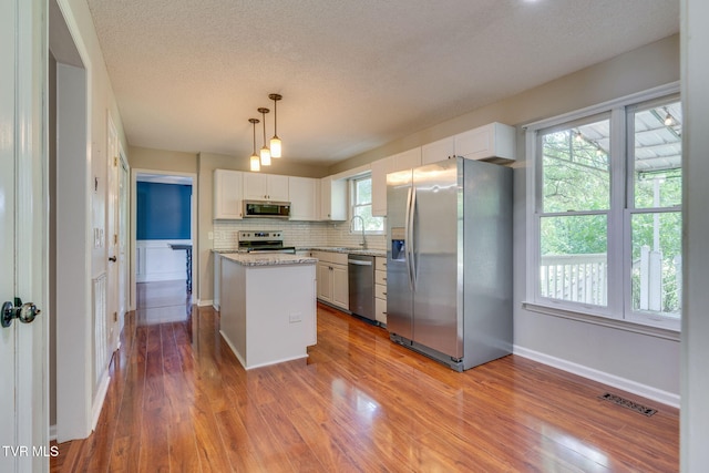219 Meridale Dr, Johnson City, TN 37601 - kitchen featuring appliances with stainless steel finishes, a center island, wood finished floors, decorative backsplash, and a textured ceiling