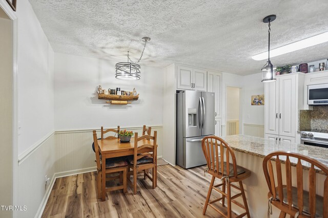 5009 Surrey Dr, Kingsport, TN 37664 - dining space with light wood finished floors, a wainscoted wall, a chandelier, and a textured ceiling