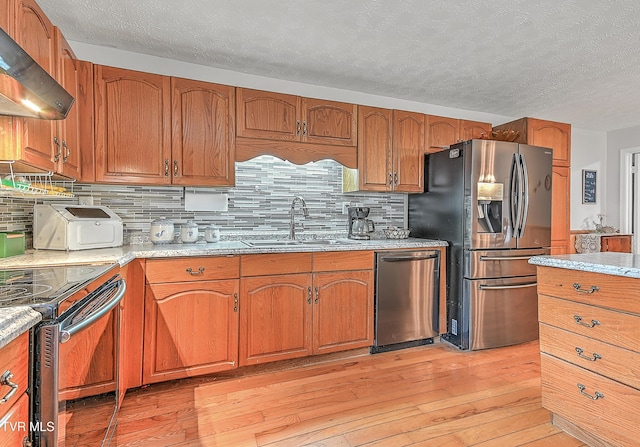 481 Pleasant Hill Rd, Blountville, TN 37617 - kitchen featuring wall chimney range hood, stainless steel appliances, a sink, light wood-type flooring, and brown cabinets