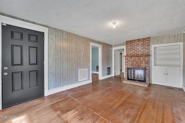 1217 Kentucky Ave, Bristol, TN 37620 - unfurnished living room featuring a textured ceiling, wood finished floors, a fireplace, wooden walls, and baseboards