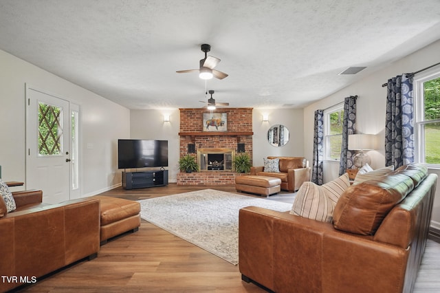 8466 Courtland Rd, Wise, VA 24293 - living area with light wood-type flooring, a ceiling fan, a textured ceiling, a brick fireplace, and baseboards