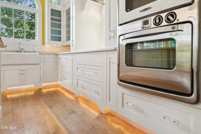 133 Knob Creek Dock Rd, Johnson City, TN 37601 - kitchen featuring oven, white cabinetry, glass insert cabinets, a sink, and light wood-style flooring
